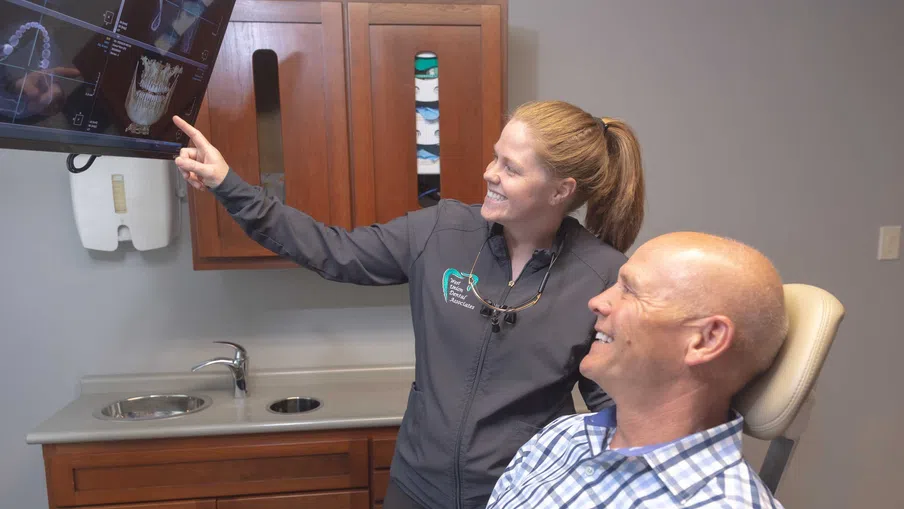 Dentist explains dental X-rays to smiling male patient in a modern dental office examination room.