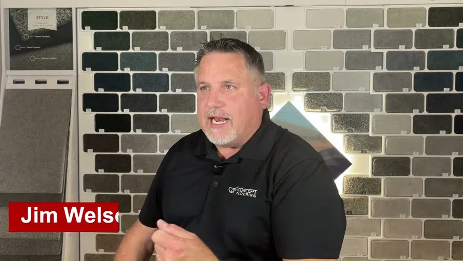 Man in black CF Concept Flooring shirt discussing tile samples on wall behind him in a showroom.