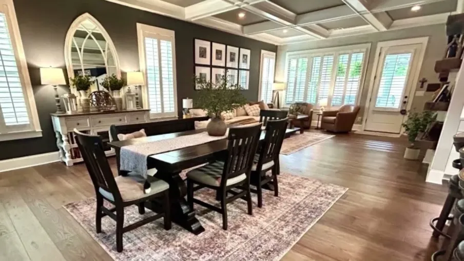 Bright open living and dining room with dark furniture, large windows, hardwood floors, and decorative accents.