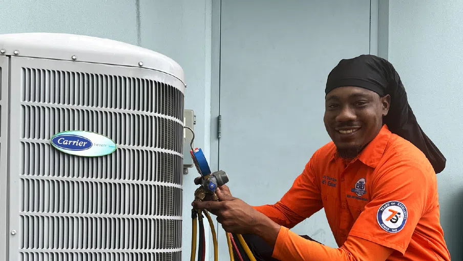 Estes Services Technician in orange uniform servicing a Carrier air conditioning unit with colored gauge hoses.