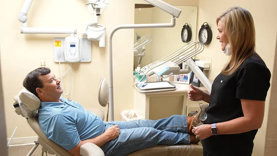 Patient smiling in dental chair while dentist talks to him in a bright, modern dental office.