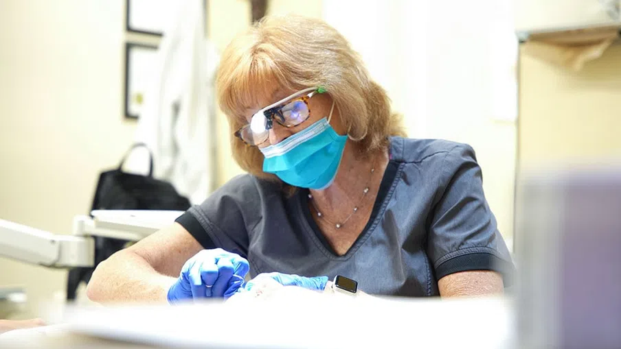 Female dentist wearing protective glasses and mask performing dental procedure with gloves in clinic.