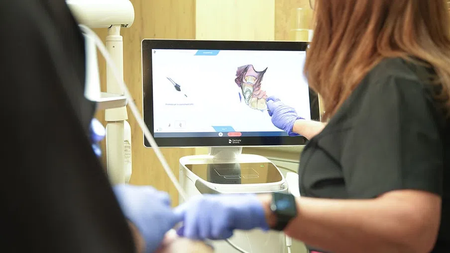 Dental professional pointing at 3D oral scan on computer screen during patient consultation.