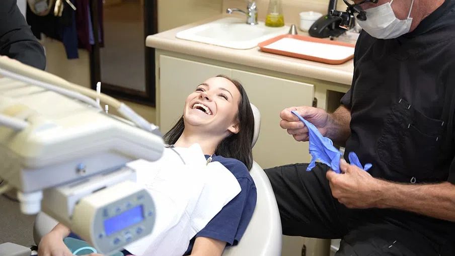 Young woman smiling in dental chair while dentist puts on blue gloves in clinic setting
