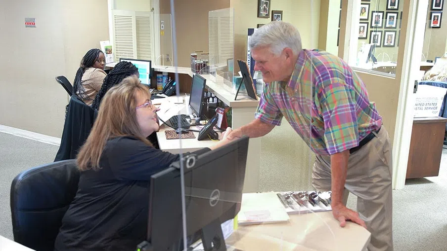 Man shaking hands with receptionist at an office desk with computers and paperwork around them.