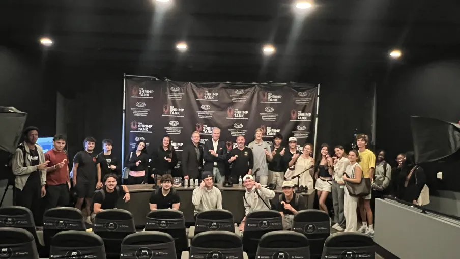 Group photo of people posing in a theater with a black backdrop featuring The Shrimp Tank logos