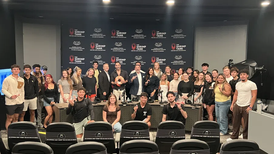 Group of people posing in front of a backdrop with The Shrimp Tank logos inside a conference room