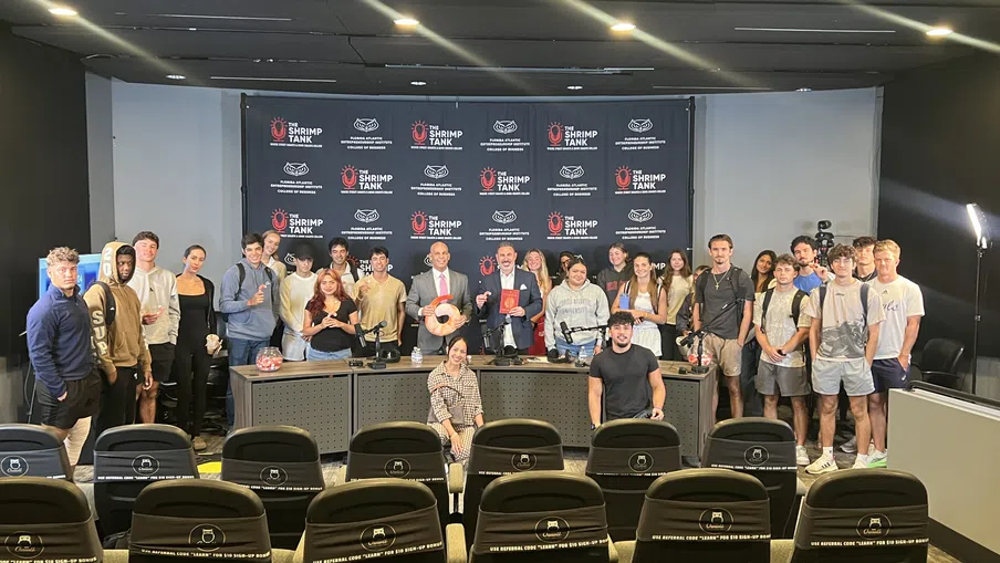 Group photo of young adults and presenters on stage at The Shrimp Tank event in a modern conference room.