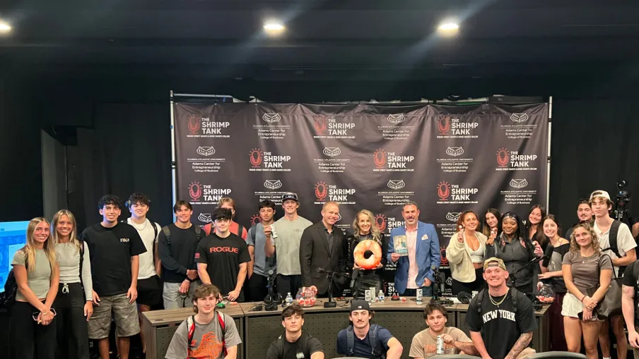 Group photo of young people and adults at The Shrimp Tank event with branded backdrop and chairs in foreground.
