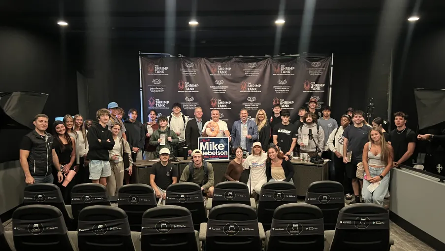 Large group of people posing in a theater room with film sponsor banners behind and empty theater seats in front