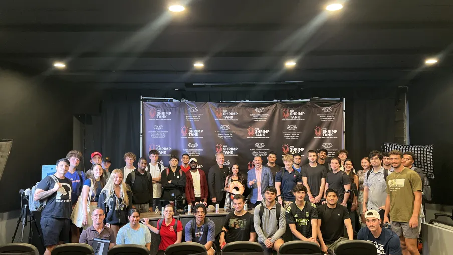 Large group of diverse people posing in a conference room in front of a black backdrop with Shrimp Tank logos.