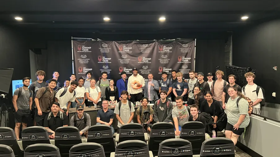 Group photo of diverse young adults posing in a theater with Shrimp Tank branded backdrop behind them