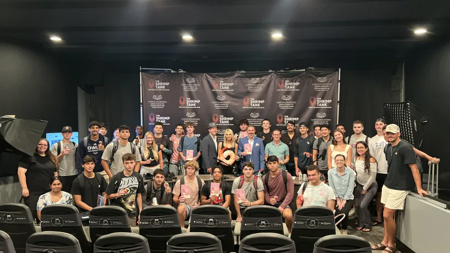 Group of young people posing in a theater with a Shrimp Tank backdrop and theater chairs in front.