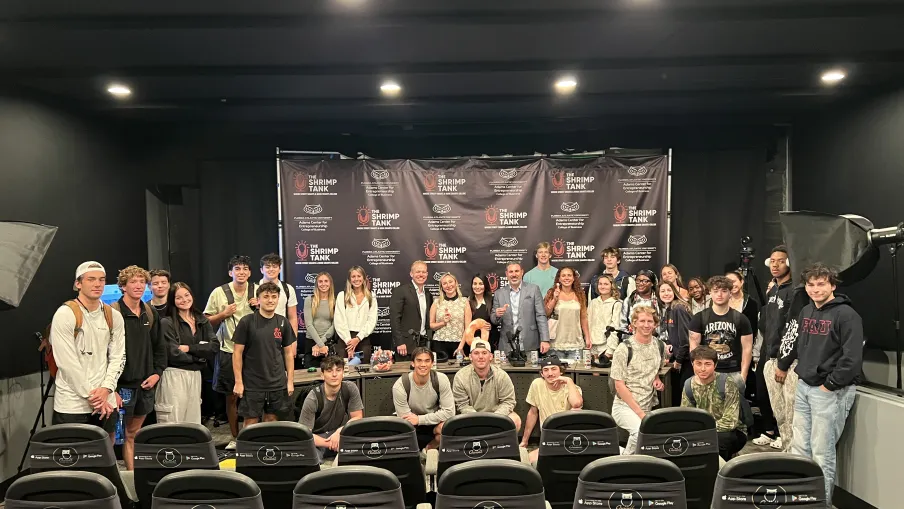 Large group of young adults and professionals posing in a conference room in front of Shrimp Tank event backdrop.