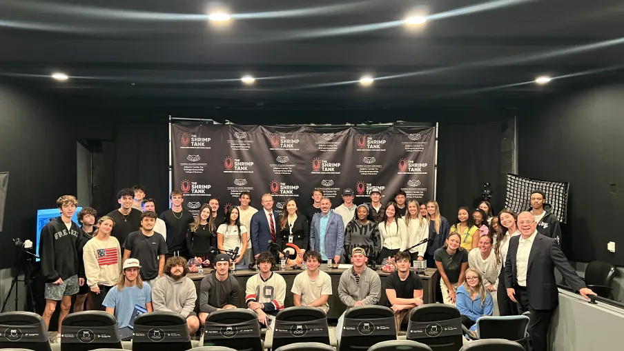 Large group of diverse young adults and professionals posing in a studio with Shrimp Tank branded backdrop.
