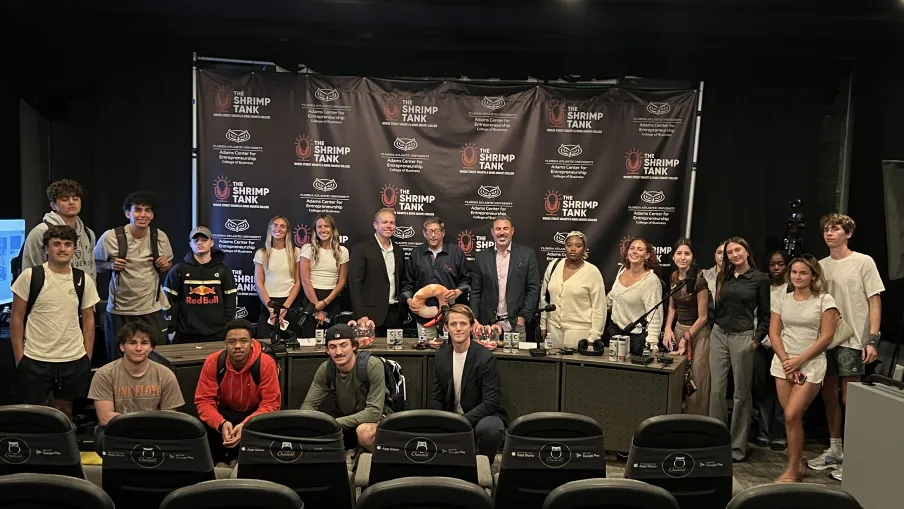 Group photo of young adults and professionals at The Shrimp Tank event with branded backdrop and tech gadgets.