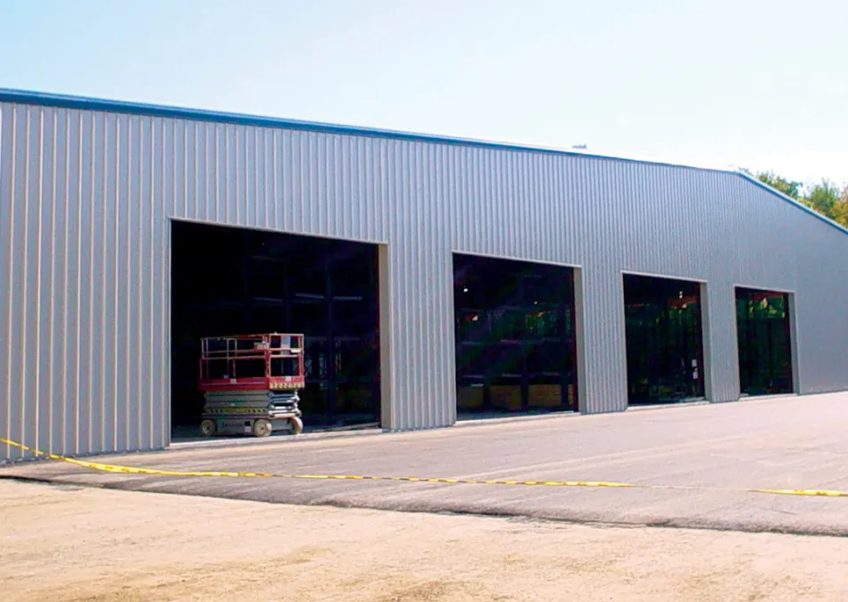 Large industrial metal warehouse with open bays and construction equipment parked inside on a sunny day