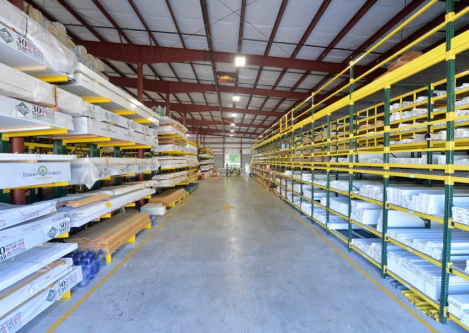 Spacious warehouse aisle with organized shelves stocked with lumber and construction materials under bright lighting.