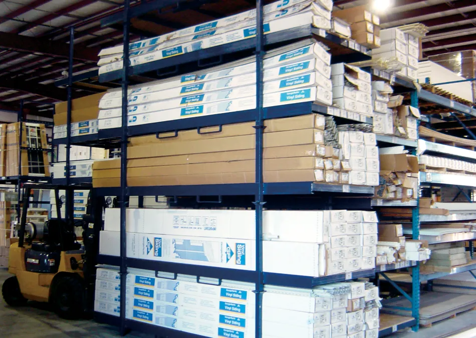 Warehouse shelves stocked with boxed vinyl siding panels and a forklift next to the storage racks.