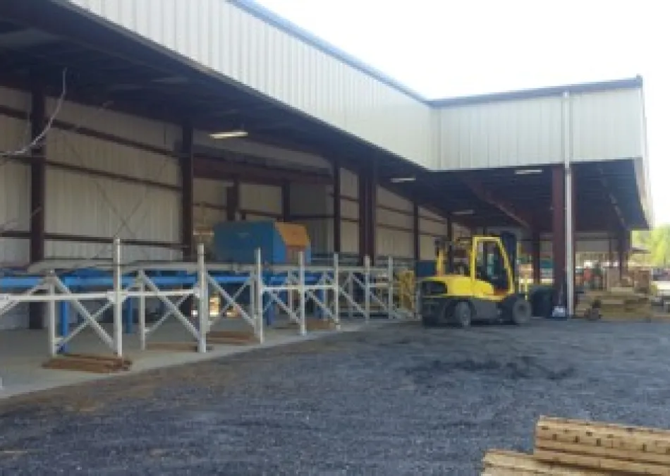 Industrial warehouse exterior with forklift and conveyor system on a gravel surface under metal roofing