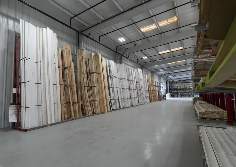 Spacious warehouse aisle with stacks of various wooden planks and building materials organized on racks.