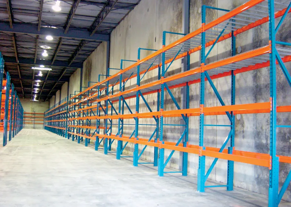 Empty warehouse shelving racks with orange beams and blue supports inside a large industrial building.