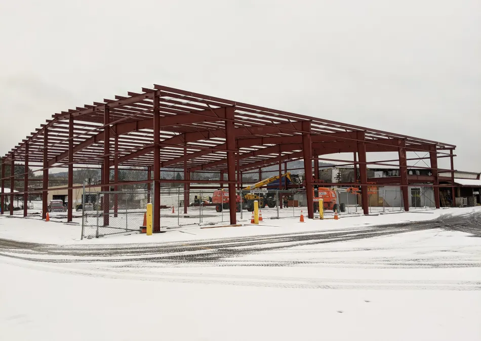 Steel frame structure of a building under construction surrounded by snow and construction equipment.