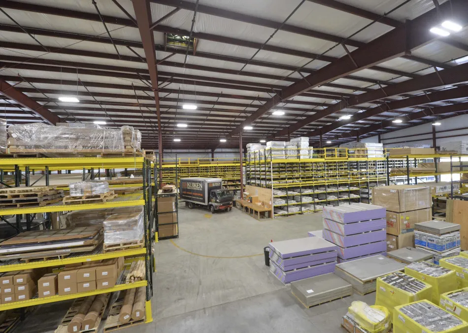 Large warehouse interior with yellow shelving, stacked pallets, and a delivery truck inside a spacious industrial building.