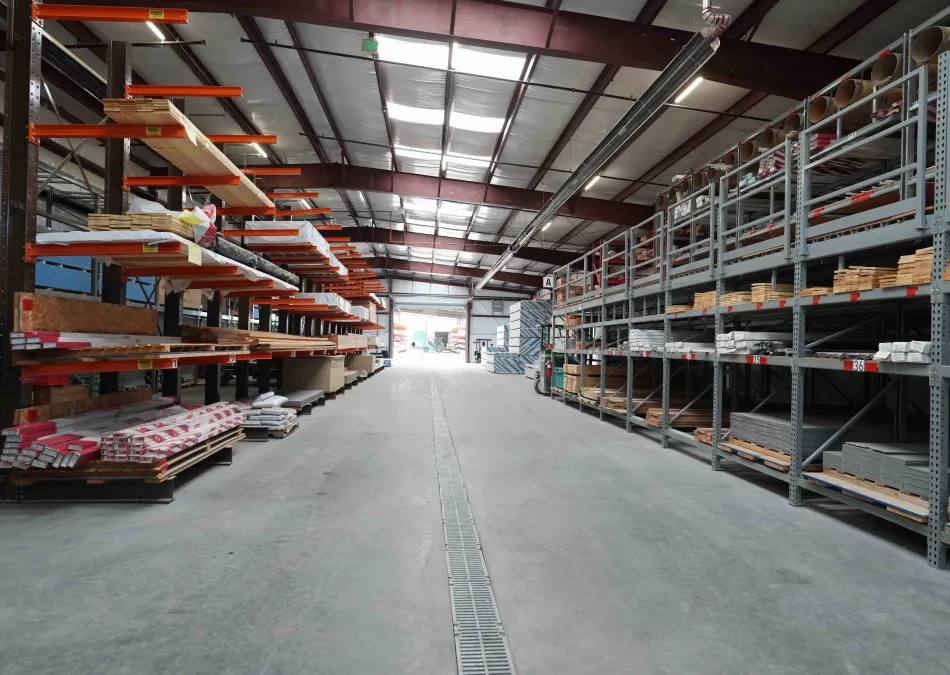 Spacious warehouse aisle with metal and wood shelves stocked with construction materials under a high ceiling.