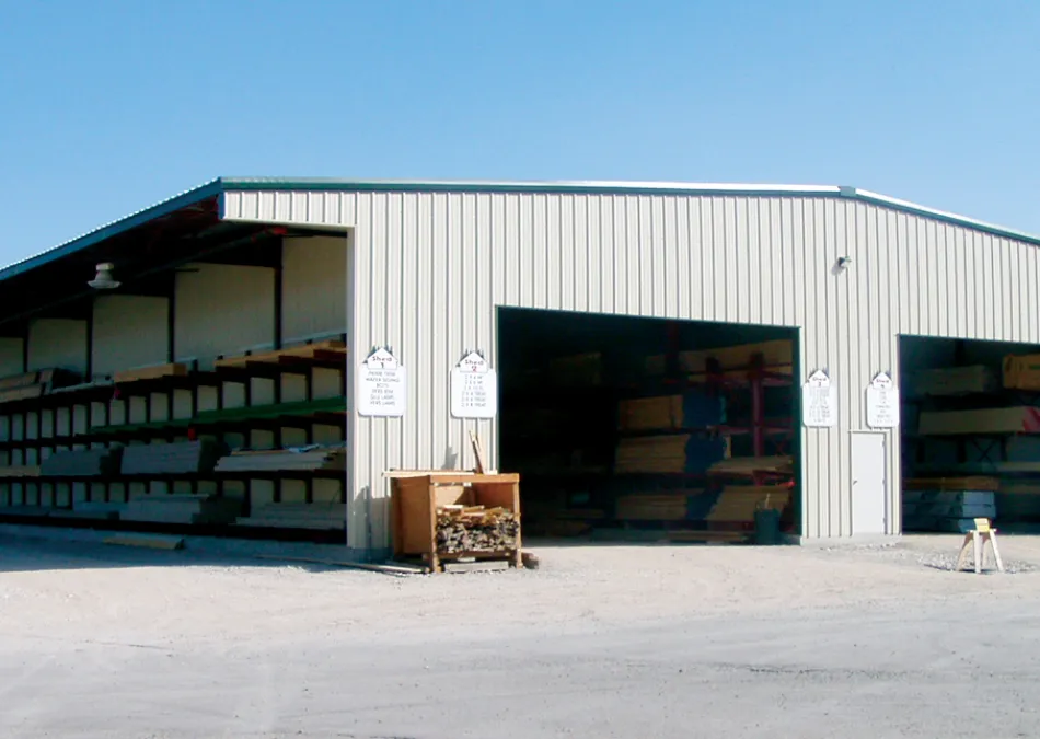Large outdoor lumber storage shed with wood planks organized on shelves under a clear blue sky.
