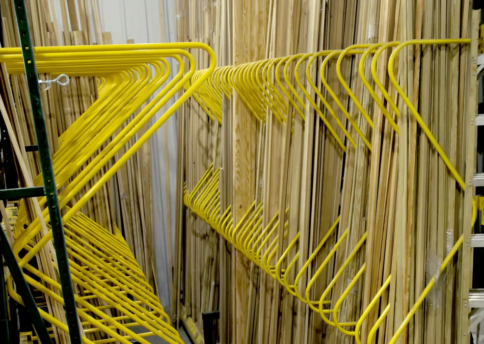 Yellow metal racks holding long wooden planks neatly organized in a warehouse aisle under bright lights