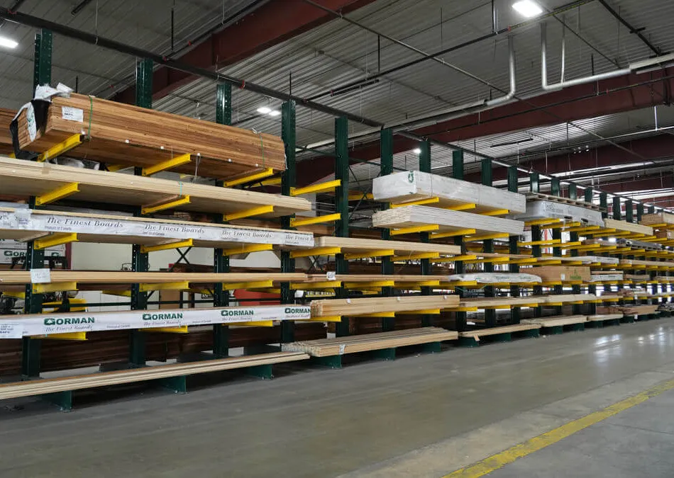 Warehouse interior with organized wooden lumber stacked on metal racks under industrial ceiling.