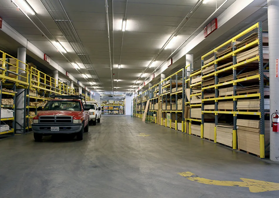 Spacious warehouse aisle with shelves stocked with lumber and parked pickup trucks in industrial setting