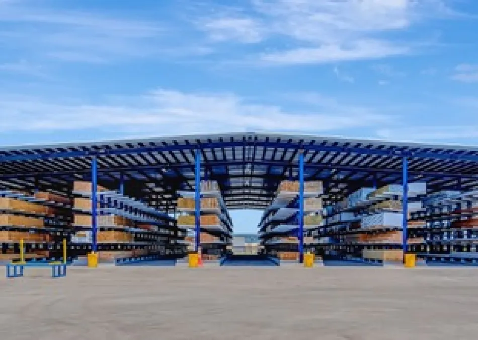 Open-air warehouse with blue steel racks holding large construction materials under a clear sky.