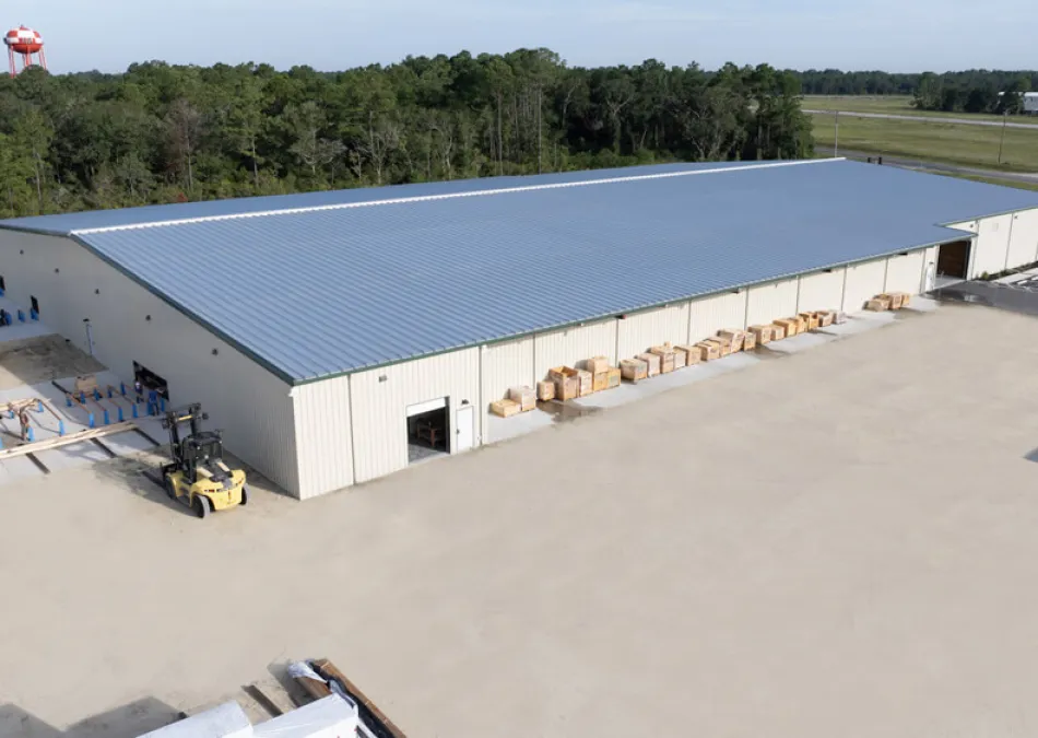 Large industrial warehouse with metal roof, forklift, and stacked wooden pallets in a spacious outdoor yard.