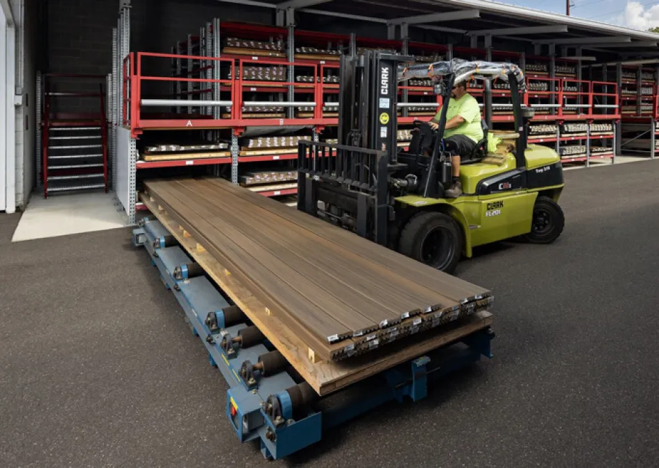 Worker operating forklift moving metal sheets in an industrial outdoor storage area with shelves.