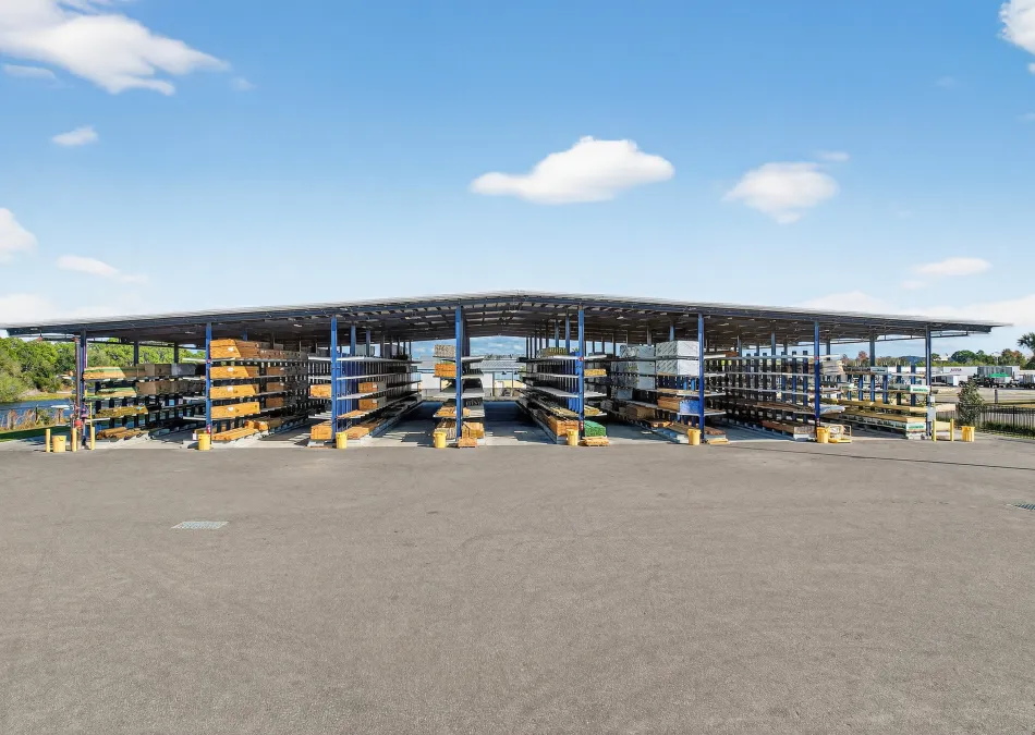 Outdoor covered storage racks holding various lumber and building materials under a clear blue sky.