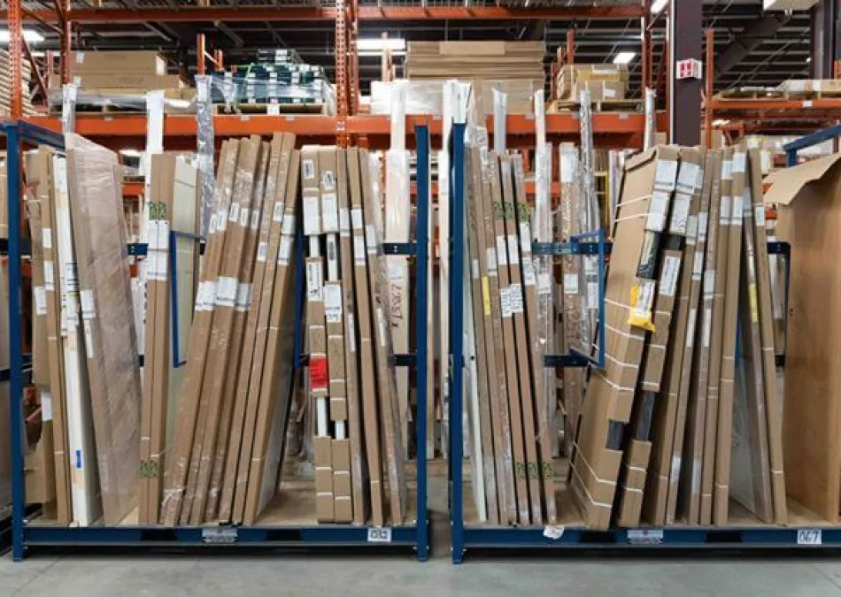 Warehouse shelving filled with tall, boxed items like doors, panels, and frames organized in rows.