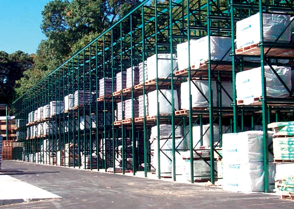 Large outdoor warehouse racks stacked with pallets of packaged goods under a clear sky with surrounding trees.