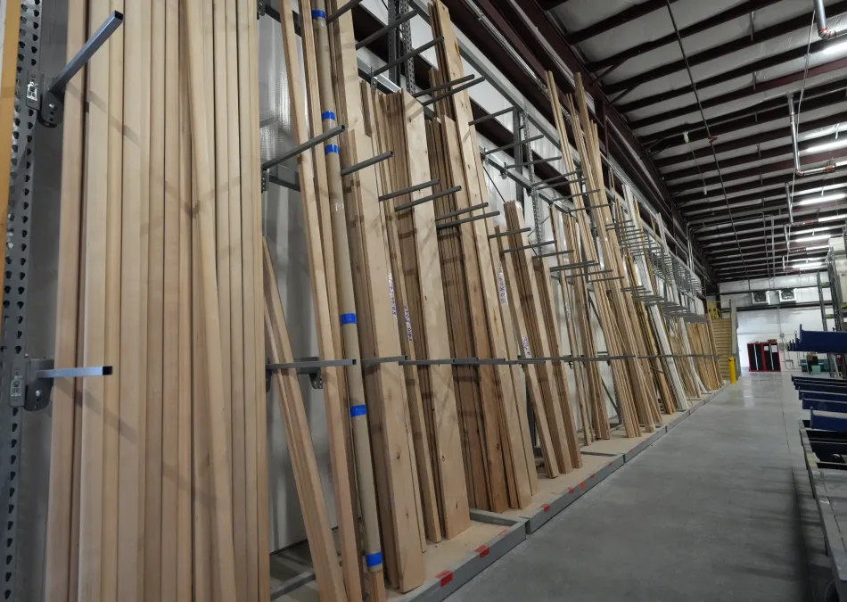 Rows of various wooden planks and boards neatly stored on vertical racks inside a spacious warehouse.