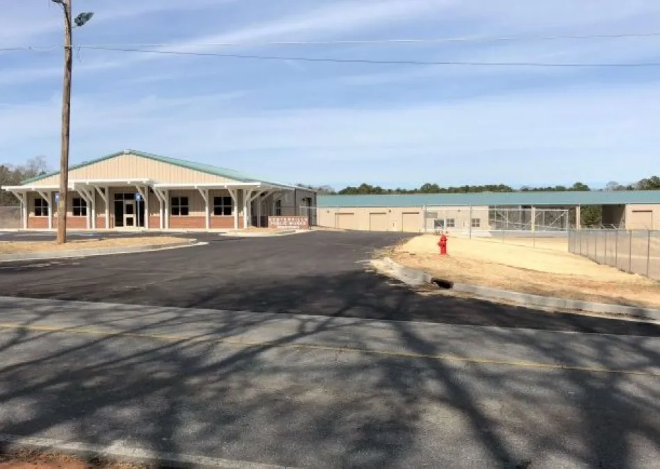 Newly paved driveway leading to modern building with green roof and adjacent storage units under clear sky.