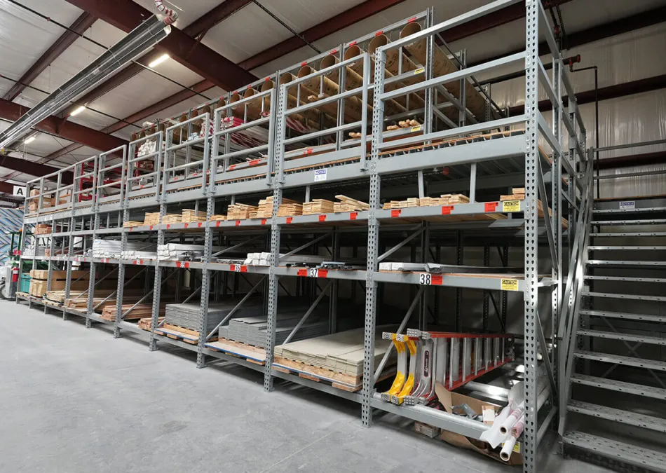 Large metal industrial shelving storing wood planks, boxes, ladders, and construction materials in a warehouse
