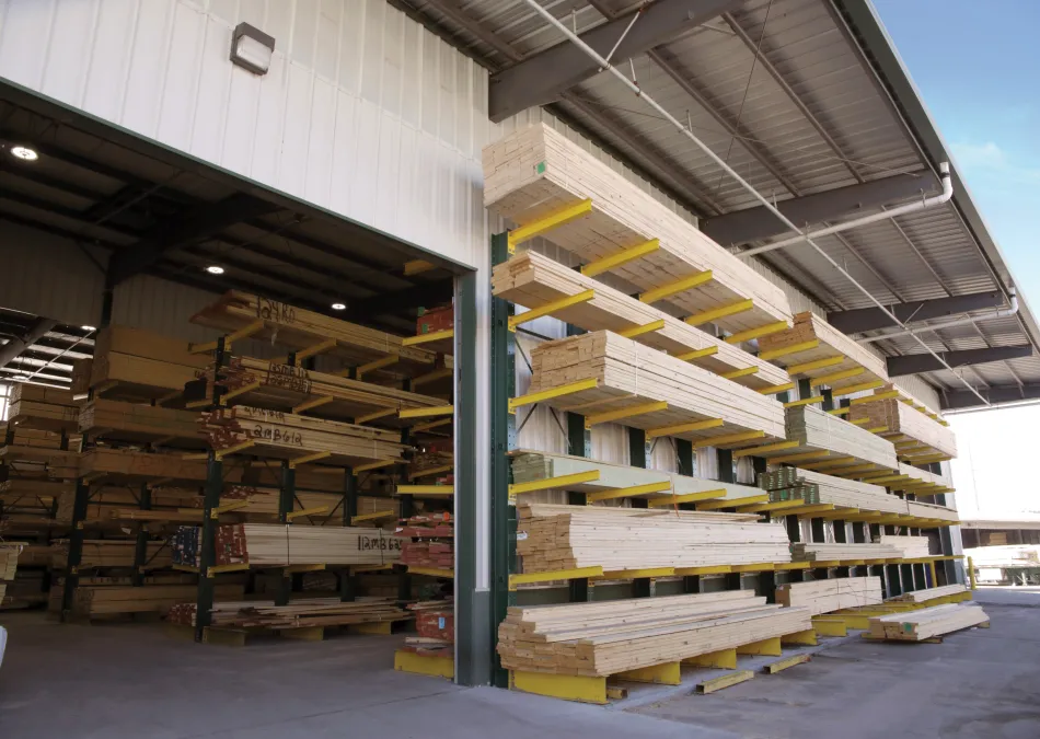 Stacks of lumber neatly organized on yellow racks inside and outside a covered warehouse under a clear sky