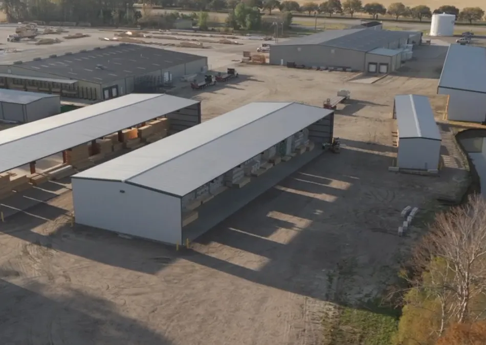 Aerial view of multiple large industrial warehouses and storage buildings with surrounding dirt roads and trees.