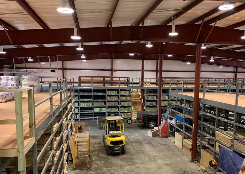 Wide view of a warehouse interior with metal shelving, stocked goods, a yellow forklift, and a pickup truck.