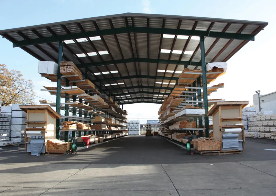 Outdoor lumber storage with metal roof and stacked wooden planks on shelves in a lumberyard.