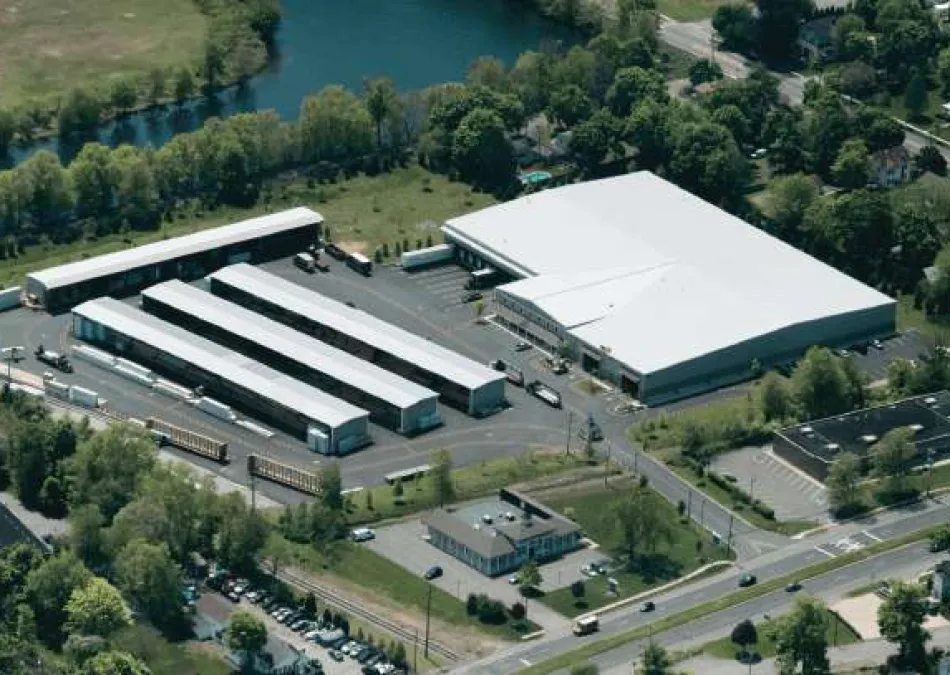 Aerial view of an industrial warehouse complex with multiple loading docks and parked semi-trailers surrounded by greenery.