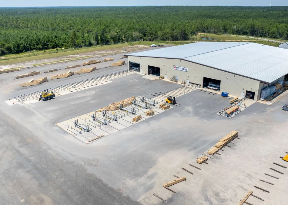 Aerial view of a large industrial warehouse surrounded by stacks of lumber and equipment in a clearing.