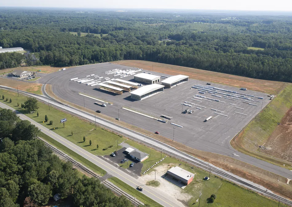 Aerial view of a large bus depot with multiple buses parked and surrounded by forest and roads.