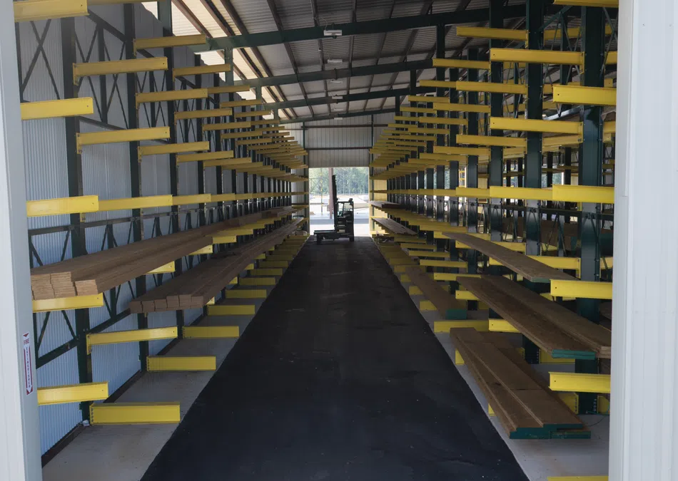 Warehouse aisle with yellow cantilever racks storing wooden planks inside a covered industrial building.